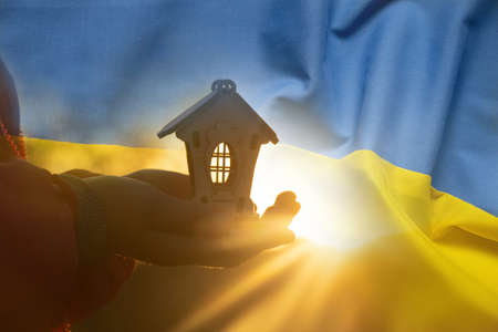 The national flag of Ukraine is yellow-blue on the background of children's hands holding a wooden small house, peace and family in Ukraine, home 2022の写真素材
