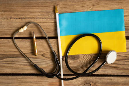 The flag of Ukraine lies with a bullet and a stethoscope on a wooden table, military medicine in Ukraine at warの写真素材