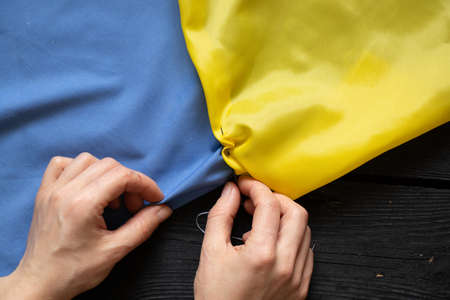 Female hands of a Ukrainian woman sew the national flag of Ukraine yellow-blue at the table at home in Ukraine, patriot, stop the war in Ukraine 2022の写真素材