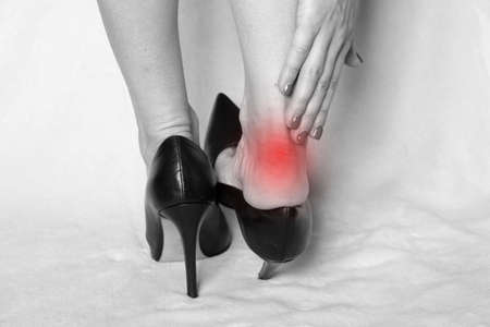 Legs of a girl in high-heeled shoes holding on to a leg that hurts on a white background, tired legs and uncomfortable shoes, fashion victim, legs hurtの写真素材