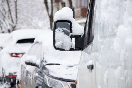 Parked cars on the roadside along the houses in the morning on the street in the city in the snow, the city of Dnipro in Ukraine, winter weather in the cityの写真素材
