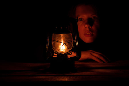 Young Ukrainian girl with a kerosene lamp in the dark sits at home without lightの写真素材