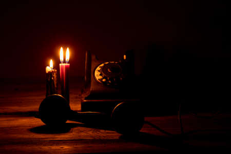 Old black retro telephone on a wooden table in the dark near the flame of candles, telephone and...
