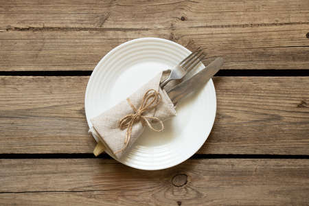 One white plate and a fork with a knife lie on an old wooden table in the kitchen at home, restaurant business, kitchen appliancesの写真素材