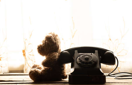 Children's teddy bear sits near the old telephone at home and is sad, retro phone