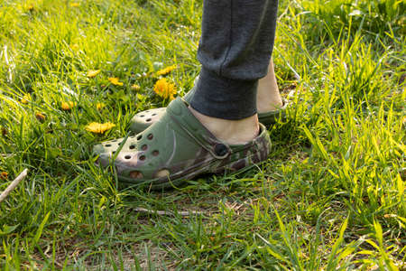 Women's feet in plastic summer shoes for water recreation, camouflage summer beach shoes in the sun...