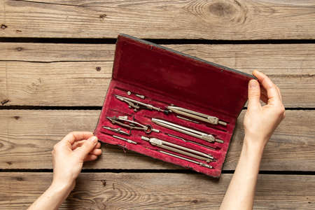Old drawing compasses in a red box on the table in the hands of a girl, school and education,...