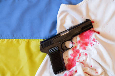 The gun lies on a bloody female dress on the flag of Ukraine, war in Ukraine, weapons, violence...