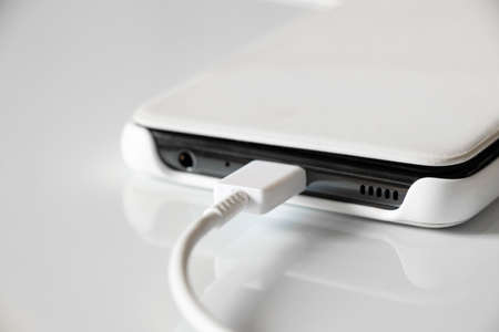 White mobile phone in a case lies on recharging on a white background, USB cable and phone close up, fast phone chargingの写真素材