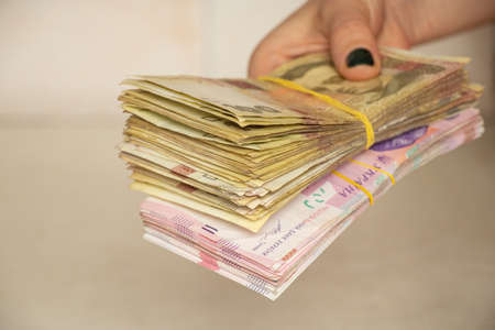 A woman's hand holds a stack of Ukrainian hryvnias, giving money, one hundred and two hundred...