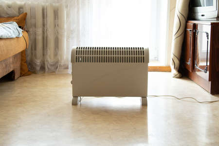 A heating convector stands in the middle of a bedroom in an apartment in the daytime in the sun, a convector in an apartment, a household heaterの写真素材