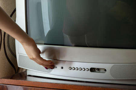 A woman's hand turns on an old gray TV in an apartment at homeの写真素材