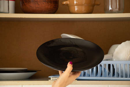 The girl takes out a plate from the shelf of the kitchen cabinet, a kitchen cabinet with dishes in...