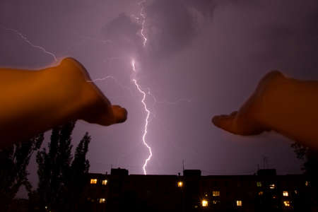Women's hands are stretched out to the sky against the backdrop of lightning over the city and houses at night, a prayer to God during a thunderstorm, lightning over a city in Ukraineの写真素材