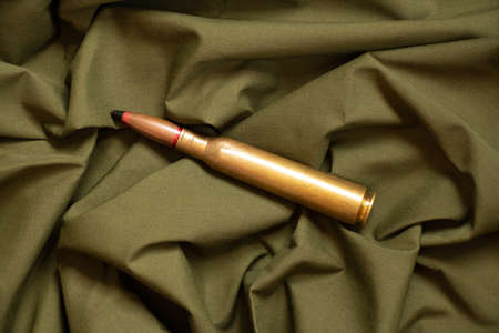 One bullet lies on a green camouflage background, military weapon, ammunition depot