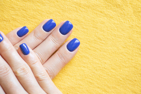 Manicure and blue polish on the girl's finger on a yellow background, yellow-blue color of the flag of Ukraine, gel polish on the girl's nails, manicureの写真素材