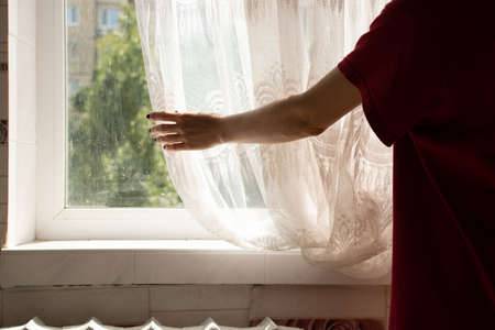 The girl closes the curtains with her hand near the windows in the apartment, open the curtains with her handの写真素材
