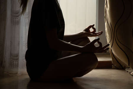 The girl meditates in the apartment sitting on the floor near the window, yoga and meditation at homeの写真素材