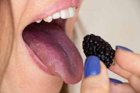 The girl eats mulberries, red tongue from mulberries, mouth and tongue, eat berriesの写真素材