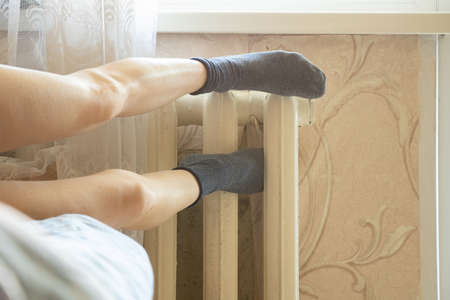 Women's feet in socks on an old cast-iron battery in an apartment in winter, a cold apartment, a heating season, a battery in an apartment, it's coldの写真素材