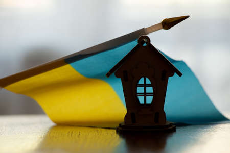 A small wooden house and the flag of Ukraine stands at home on the table in the dark, home Ukraine, war 2022の写真素材