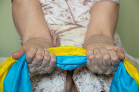 An old woman holds the flag of Ukraine in her hands at home in Ukraine, stop the war
