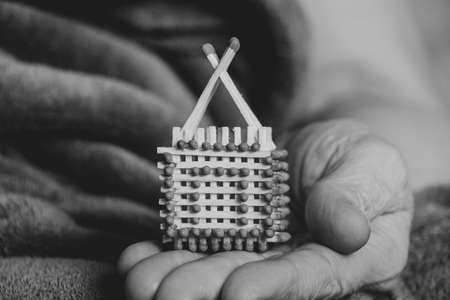 A small match house in the hands of an old woman, a homemade house made of matches