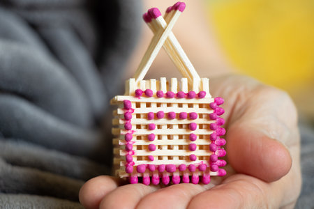 A small match house in the hands of an old woman, a homemade house made of matches