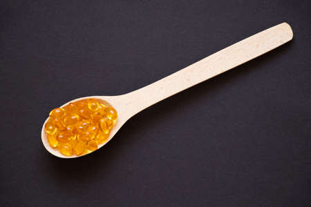 Fish oil pills lie in a wooden spoon on an isolated background, vitamins and supplementsの写真素材