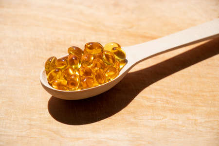 Fish oil pills lie in a wooden spoon on an isolated background, vitamins and supplementsの写真素材