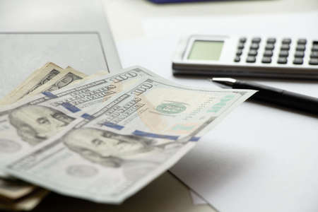 One hundred dollars lie on a laptop on the table and next to it lies a calculator and a pen, business and financeの写真素材