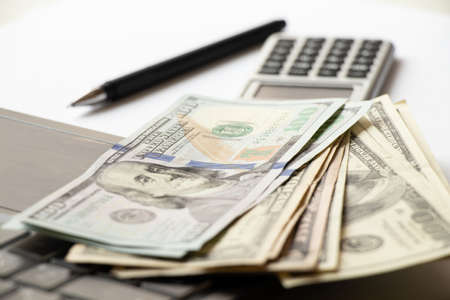 One hundred dollars lie on a laptop on the table and next to it lies a calculator and a pen, business and financeの写真素材