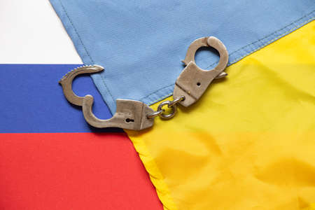 Ukrainian and Russian flags and handcuffs lie in the middle, law and justiceの写真素材
