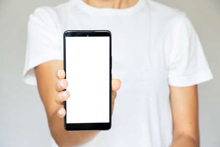 A girl in a T-shirt on a white background in her hand holds a mobile phone with a white screen, a...