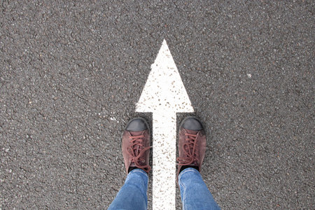Women's feet stand on the forward arrows on the road, sneakers on the road and the road forward arrow, start and startの写真素材
