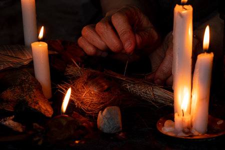 Voodoo doll in the hands of an old witch with a needle in her heart in the dark against the background of candles, curses and black magicの写真素材