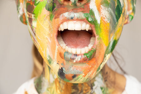 A girl with a face painted with paints with her mouth wide open, teeth and mouth, screamingの写真素材