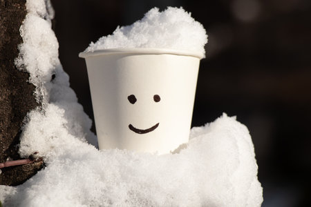 a paper white glass in the snow and a smile is painted on itの写真素材