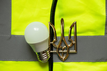 LED lamp and coat of arms of Ukraine lie on a reflective vest, Ukraine without light, energy crisis, warの写真素材