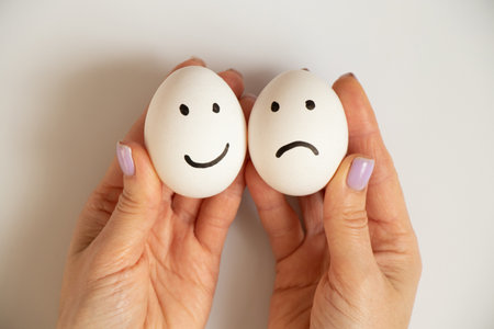 Two eggs with a joyful smile and a sad one in the hands of a girl on a white background, joy and sadness choice, lunchの写真素材