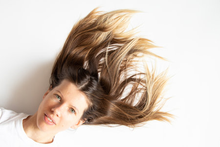 A girl with long hair and a smile lies on a white background, an emotion of happiness, hair careの写真素材
