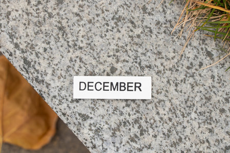 December is written on a wooden white board which lies on a stone road in the street, a calendar as...