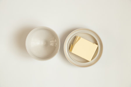 A piece of butter lies in a white plate on a white background close-upの写真素材
