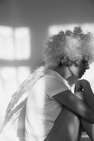 Girl in an angel costume with wings and curly hair on an isolated background with shadows on the wallの写真素材