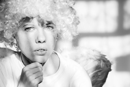 Girl in an angel costume with wings and curly hair on an isolated background with shadows on the wallの写真素材