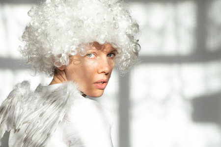 Young girl in an angel costume with wings and curly hair on an isolated background with shadows on the wallの写真素材
