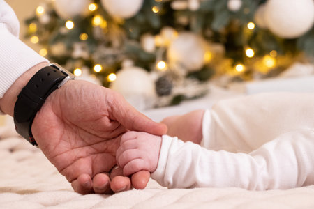 Dad's hand holds the hand of a newborn under the New Year tree, love, the hand of a newbornの写真素材