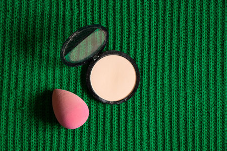 Powder and sponge for makeup lie on a green cloth, cosmetics and fashion, makeup artist