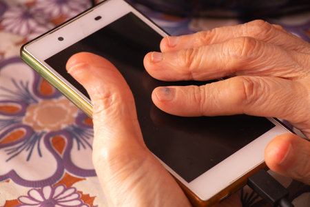 elderly woman holding a phone in her hands while sitting at a table in the kitchen closeup