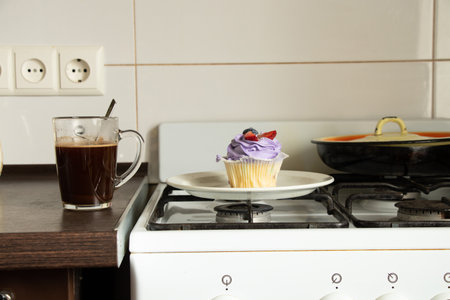 One muffin stands on a gas stove and next to it is a cup of coffee in the kitchen for breakfast at home, dessert and coffeeの写真素材